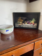 Laden Sie das Bild in den Galerie-Viewer, A framed still life painting depicting a dark barrel, autumn leaves, and vegetables, displayed on a wooden desk next to a ceramic bowl. Frame is a simple black wood.