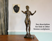 Cargar imagen en el visor de la galería, Bronze statue of a nude figure on a wooden pedestal against a white wall with another bronze hanging on the wall. Both bronze sculptures by Kelly Borsheim