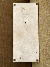 Load image into Gallery viewer, A rectangular beige travertine stone wall plate or backplate with pre-drilled screw holes and corner brackets, shown on a textured brown woven fabric background.