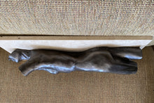 Load image into Gallery viewer, A dark bronze-finished figurative sculpture of a reclining human figure, displayed horizontally on a textured beige woven rug bench seat.