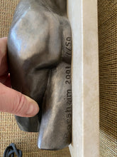 Load image into Gallery viewer, Close-up of a hand holding a dark gray bronze sculptural object detail showing engraved text reading 'Borsheim 2001 7/50' mounted to a light beige stone on a beige upholstered bench.