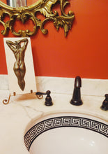 Load image into Gallery viewer, Shown here is the Ten female nude bronze bas - relief in a bathroom of black and white marble countertop, red painted walls, and a classic style bronze framed mirror
