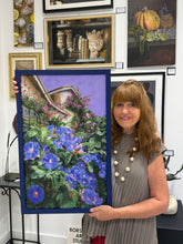 Laden Sie das Bild in den Galerie-Viewer, A female artist wearing a gray pleated dress holds up a large framed painting of blue morning glories and green foliage against a purple sky, set in an art gallery with other framed paintings on the wall.