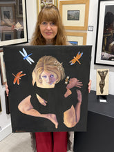 Charger l'image dans la galerie, A woman holding a large black canvas painting featuring a stylized portrait of a woman with dragonflies, photographed in an art gallery with framed paintings in the background.