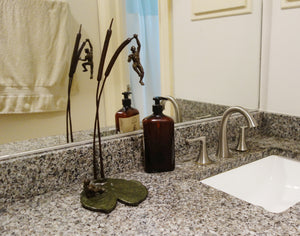 Tabletop bronze sculpture of two men on a lily pad and two cattails is shown here is a man's bathroom.  Reflected in the mirror, one sees the pose from two different points of view.