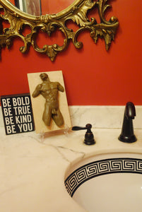 Bold decor in the bathroom of bright red, and black and white patterns show off a classical nude male body sculpture on the marble countertop