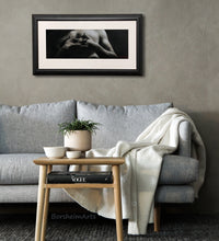 Load image into Gallery viewer, Entwined is a charcoal and white pastel drawing on grey paper, shown here as framed with white mat, black frame, and low reflective Museum Glass. The art is shown in a cozy and yet elegant living room.
