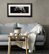 Load image into Gallery viewer, Entwined is a charcoal and white pastel drawing on grey paper, shown here as framed with white mat, black frame, and low reflective Museum Glass. The art is shown in a cozy and yet elegant living room.