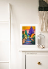 Cargar imagen en el visor de la galería, An example of framing the pastel on paper artwork Settignano Purple tree in Tuscany. Framed all in white, the colorful statement art looks great sitting on the dresser and leaning against the wall in this bedroom scene.