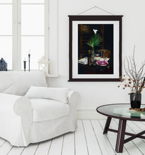 Carica l'immagine nel visualizzatore di Gallery, This dark print of an Italian table setting at night looks great framed in this mock-up of a mostly white, bathed in light, living room scene with cozy chair, window, and coffee table.