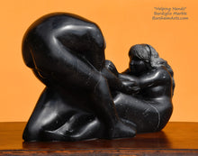 Load image into Gallery viewer, Soft face Helping Hands by Kelly Borsheim Couple Art Carved from a black Spanish marble, this sculpture depicts a man bending over forward to help a seated woman stand up. Her hands reach up towards his bearded face, but it is the moment before she is close enough to reach him. 3/4 view