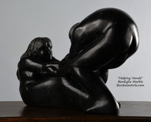 Load image into Gallery viewer, Her face and long hair Helping Hands by Kelly Borsheim Couple Art Carved from a black marble called Marquina, this sculpture depicts a man bending over forward to help a seated woman stand up.  Her hands reach up towards his bearded face, but it is the moment before she is close enough to reach him. 3/4 view of her face