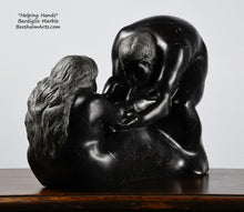 Load image into Gallery viewer, Another angle of the man's face and the woman's long hair Helping Hands by Kelly Borsheim Couple Art Carved from a black Marquina marble, this sculpture depicts a man bending over forward to help a seated woman stand up.  Her hands reach up towards his bearded face, but it is the moment before she is close enough to reach him.  view of her right side from 3/4 angle, as well as his arms and face in shadow.
