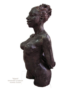 terra-cotta sculpture of a black woman with her hair pulled back into a large bun.  She stands tall and proud, her posture is slightly arched back with her arms folded together behind her, a beautiful physique