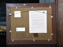 Carica l&#39;immagine nel visualizzatore di Gallery, Back of a wood-framed artwork with a certificate and text on paper taped on the back.  Wire hanging system is shows
