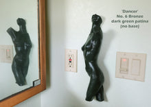 Load image into Gallery viewer, A dark green patina bronze sculpture of a dancing female figure mounted on a white wall next to a light switch and outlet, with its reflection visible in a wooden-framed mirror on the left. Text in the upper right reads 'Dancer No. 6'
