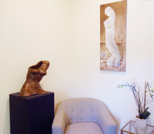 Laden Sie das Bild in den Galerie-Viewer, Ceramic female torso sculpture resting on black pedestal.  A painting of a marble statue hangs on the facing wall, with a small cushy chair and plant in the scene
