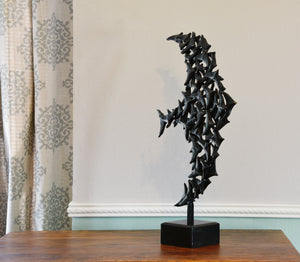 Diagonal view of a tabletop bronze sculpture on a dresser top.  Square granite base hosts the square stick that supports the bronze birds in Murmuration.