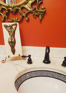 Shown here is the Ten female nude bronze bas - relief in a bathroom of black and white marble countertop, red painted walls, and a classic style bronze framed mirror