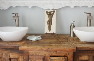 The small bronze "Ten" female nude back with arms up is displayed on a small copper easel in this rustic, but modern bathroom with his and her sinks.