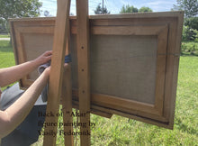 Laden Sie das Bild in den Galerie-Viewer, Back of framed painting titled &#39;Altar&#39; by Vasily Fedorouk held on an easel outdoors  by a woman.
