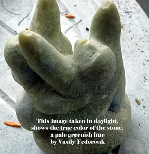 Stone sculpture of a abstracted human face looking up, arms extended on a textured surface with text overlay. Photo taken outside to better show the pale green color of the marble.  Crystal ball that rests above the figures' arms has been removed for this image.