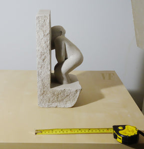 Stone sculpture of a male figure on a beige surface with a tape measure for scale.