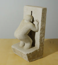 Laden Sie das Bild in den Galerie-Viewer, Stone sculpture of a figure looking through a hole in the wall. his right hand rests against the wall.  Abstracted figure art
