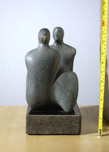 Gray stone sculpture of two figures on a white background with a tape measure for scale. side view of limestone carving by Vasily Fedorouk