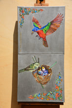 Load image into Gallery viewer, A two-panel canvas wall art set displayed on an easel against a beige wall. The top panel shows a colorful male painted bunting in flight, and the bottom panel shows a female painted bunting bird at a nest with eggs.
