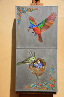 A two-panel canvas wall art set displayed on an easel against a beige wall. The top panel shows a colorful male painted bunting in flight, and the bottom panel shows a female painted bunting bird at a nest with eggs.