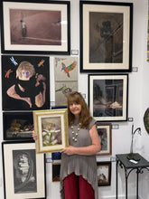 將圖片載入圖庫檢視器 A female artist stands in an art gallery holding a framed floral print with a gold frame and a bee on a Bradford Pear Tree flower. She is surrounded by many other framed artworks hanging on a white wall.
