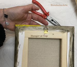 The back of the canvas has a small triangle hook to hang from the top center of the painting.  Artist's hand with bracelet and nearby a needle-nosed pliers show off the hanging system.