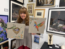 Charger l'image dans la galerie, A woman stands in an art gallery holding two square canvas paintings. The left canvas shows a green Painted Bunting bird in a nest with yellow chicks, and the right canvas shows a colorful male Painted Bunting bird with green, orange, and blue feathers.
