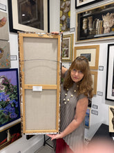將圖片載入圖庫檢視器 A woman in a gray dress holds up a large, unframed canvas painting showing its backing and stretcher bars. The setting is an art gallery with her various framed paintings and sculptures on the walls.
