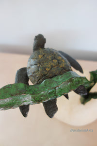 Bronze turtle sculpture on a kelp branch with a blurred background