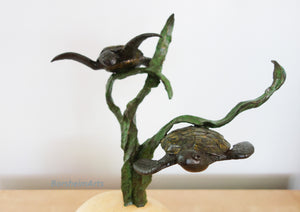 Bronze sculpture of two turtles on a three strands of sea kelp with a white background