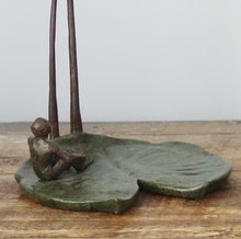 Load image into Gallery viewer, The second man in this original bronze sculpture titled &quot;The Unwritten Future&quot; is sitting on a large lily pad.  He has his hands gripping his legs to balance his body as he looks up to the swinging figure of the other man. Small tabletop sculpture detail image
