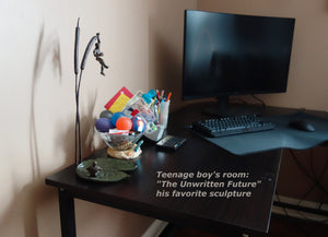 A teenage boy loves the bronze sculpture "The Unwritten Future" enough that he added it to his computer table where he loves to be a gamer.