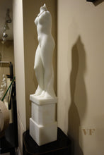 Laden Sie das Bild in den Galerie-Viewer, White marble statue of a standing female figure on a pedestal against a beige wall.
