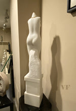 Laden Sie das Bild in den Galerie-Viewer, Back view of White marble sculpture of a female torso on a black pedestal against a beige wall.
