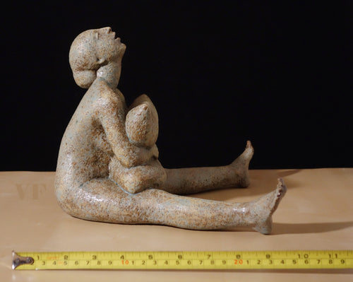 Ceramic sculpture of a seated female figure squeezing a pillow on a dark background