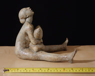 Ceramic sculpture of a seated female figure squeezing a pillow on a dark background
