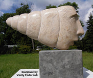 Stone sculpture of a face with shell-like patterns on a grassy background