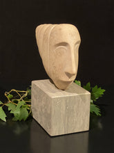 Laden Sie das Bild in den Galerie-Viewer, Stone sculpture of a thin face on a rectangular marble base with green leaves on a black background
