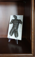 Load image into Gallery viewer, The black Valentine male figure mounted on the white marble tile is shown here resting on a clear plastic plate easel and displayed on a home bookcase.
