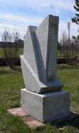 Abstract geometrical wedges stone sculpture by Vasily Fedorouk on a grassy area with power lines and trees in the background