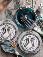 table setting This plate design features and off-center circle border (of shoes shapes) with egg-shaped balloons above the circle on the top section of the plate.  Inside is a fantasy mixture of two shoes, with elements as human hands, fruit, branches, grass, and flowers.  Mostly a black and white design.  Classic, yet Bohemian! 
