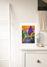 Load image into Gallery viewer, An example of framing the pastel on paper artwork Settignano Purple tree in Tuscany. Framed all in white, the colorful statement art looks great sitting on the dresser and leaning against the wall in this bedroom scene.
