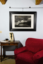 Cargar imagen en el visor de la galería, Framed Spotlight charcoal drawing of dramatic skies with sun rays dropping down on cliffs and coastline of Italy, shown here on wall in a small Tuscan living room
